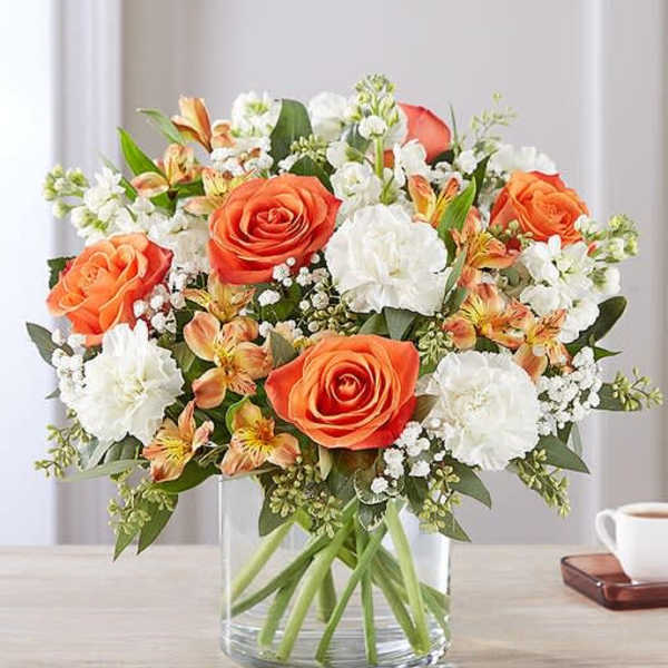 Orange roses and white flowers in a clear glass vase