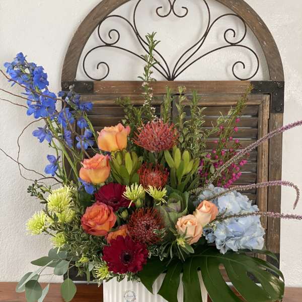 Mixed floral arrangement in a white vase with blue, orange, red, and pale blue blooms