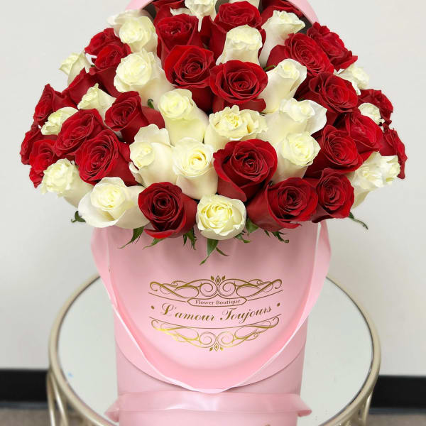 Red and white roses arranged in a pink hatbox on a small round table.