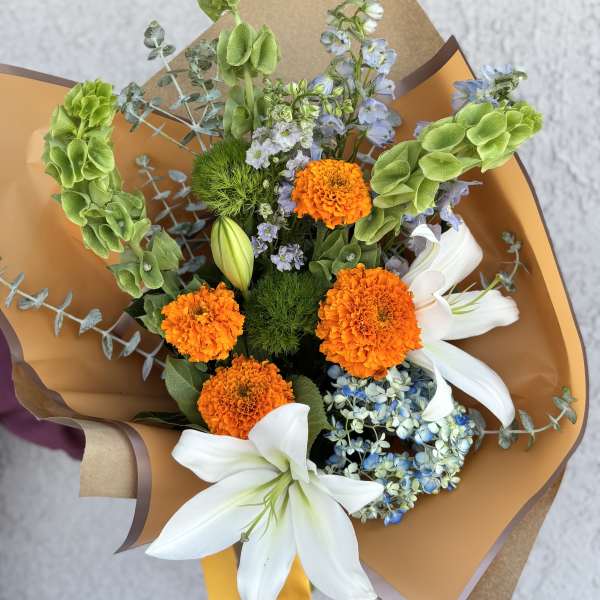 Bouquet of orange marigolds, white lilies, and blue flowers wrapped in brown paper