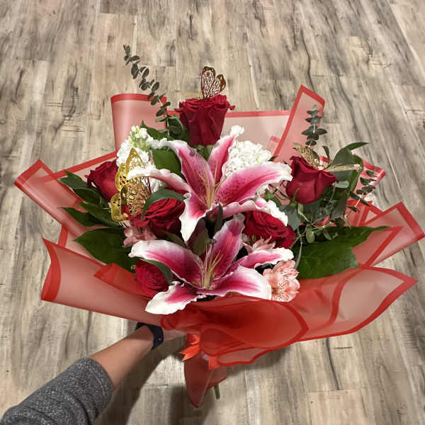 Handheld bouquet of red roses and pink lilies wrapped in red paper