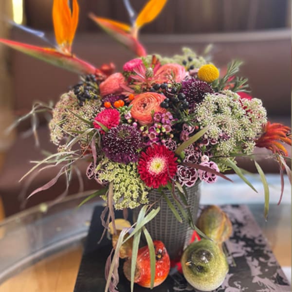 Colorful mixed flower arrangement in a dark vase with decorative bird accents