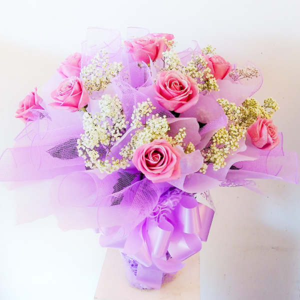 Pink roses arranged with white filler flowers and lavender ribbon wrap