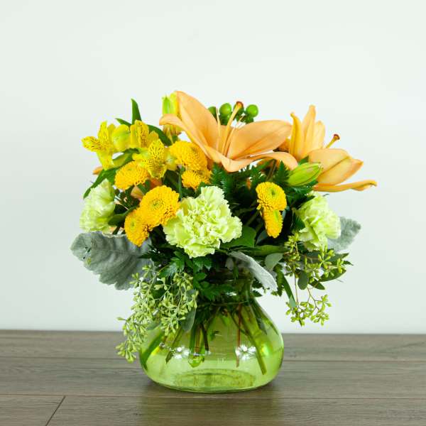 Yellow and peach floral arrangement in a green glass vase