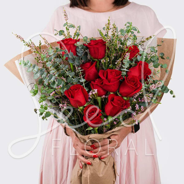 Hand-tied bouquet of red roses with eucalyptus accents wrapped in kraft paper.