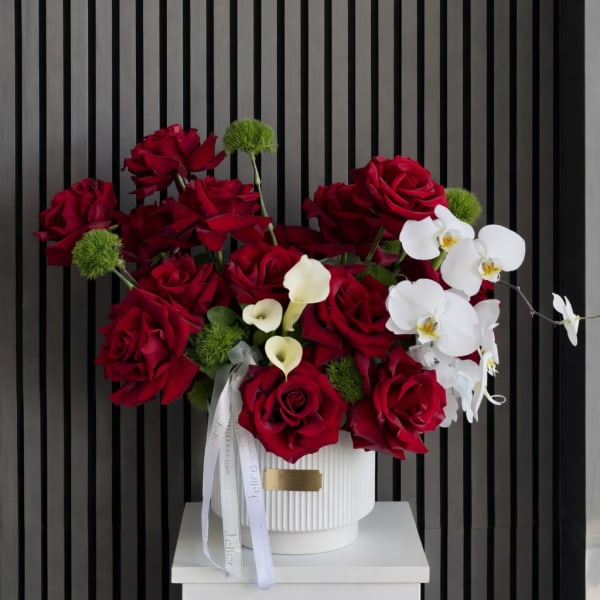 Red roses and white orchids arranged in a white vase