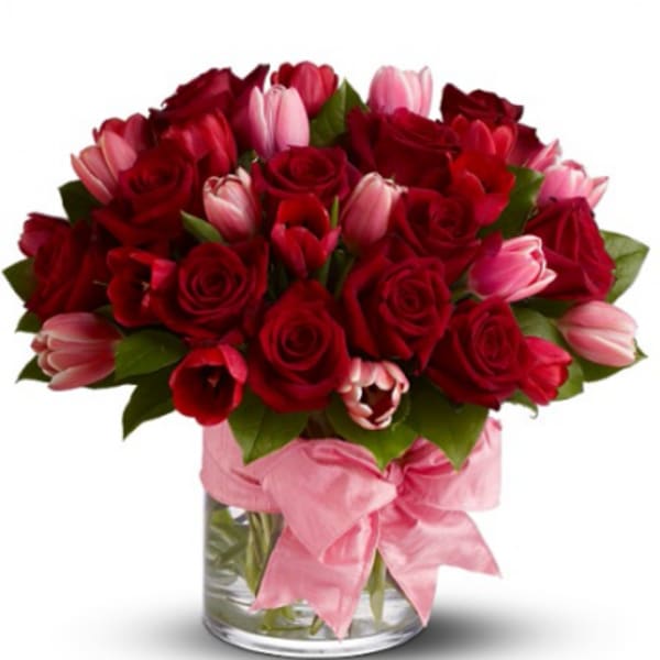 Red roses and pink tulips in a glass vase with a pink ribbon