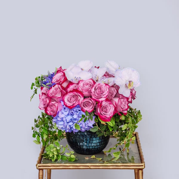 Pink roses and white orchids in a dark vase with trailing greenery