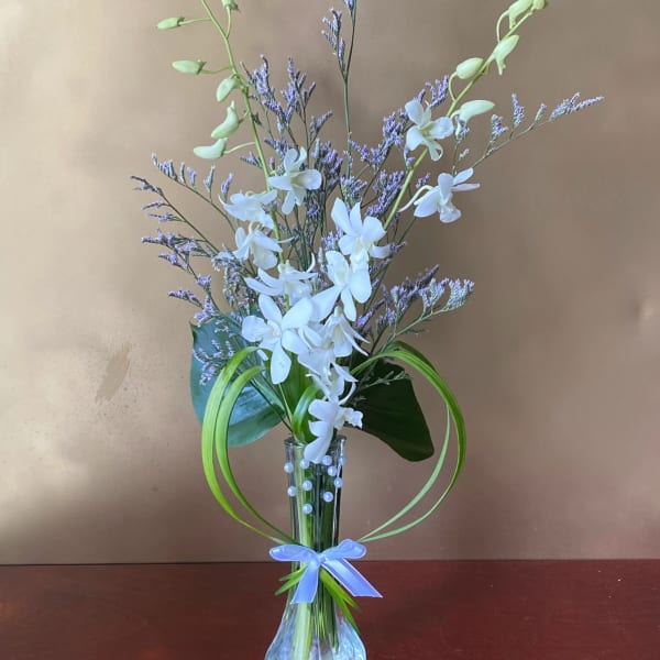 White orchids in a clear vase with purple filler flowers and a blue ribbon