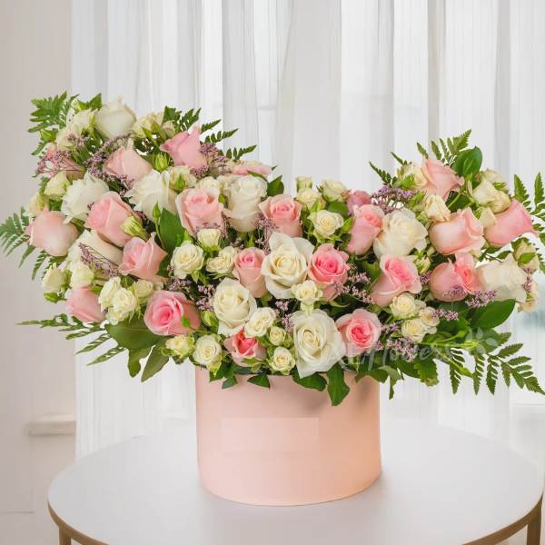 Pink and white roses arranged in a blush round box