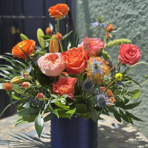 Colorful mixed bouquet in a dark blue vase with orange and pink roses