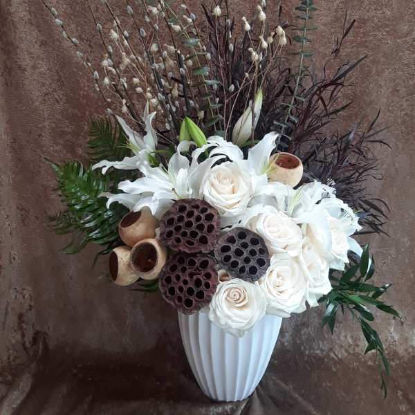 White roses and lilies in a white vase with tall branches and seed pods