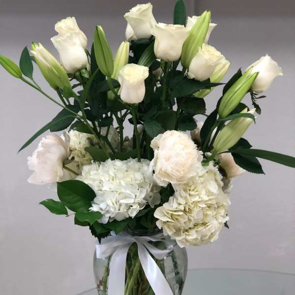 White roses and hydrangeas in a glass vase with a white ribbon