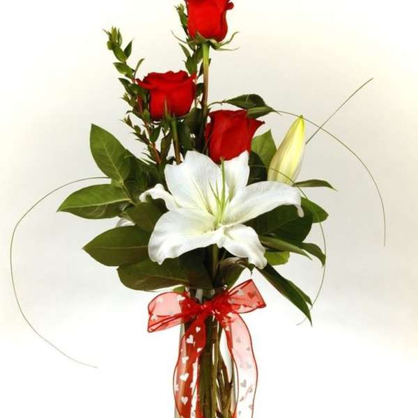 Red roses and a white lily in a clear glass vase with a red ribbon