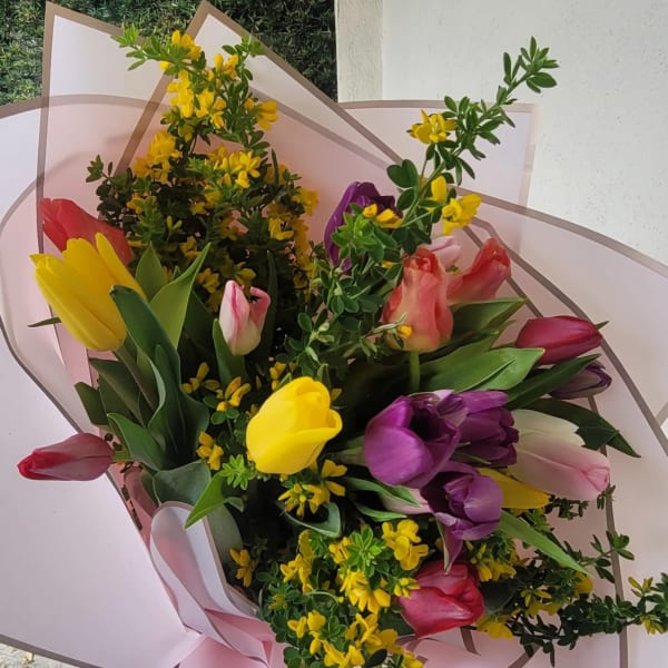 Bouquet of multicolored tulips with yellow filler flowers wrapped in pale pink paper