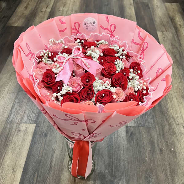 Pink and red rose bouquet wrapped in pink paper with a ribbon.