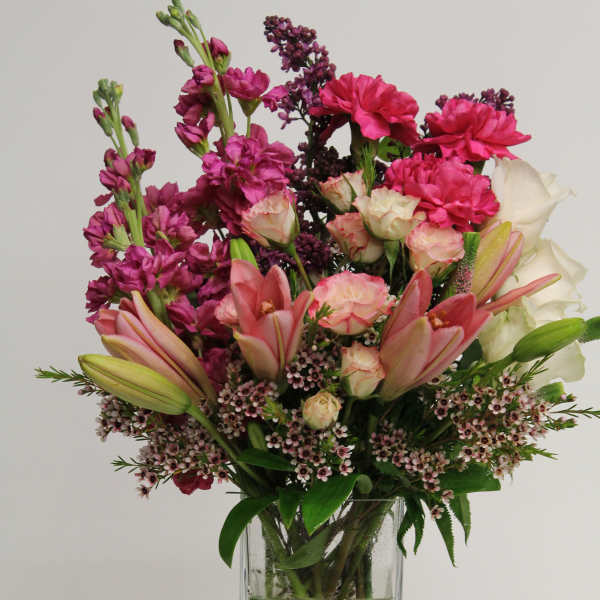 Tall arrangement of pink lilies, roses, and bright magenta flowers in a clear glass vase