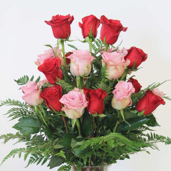 Tall arrangement of red and pink roses in a clear glass vase with a pink bow