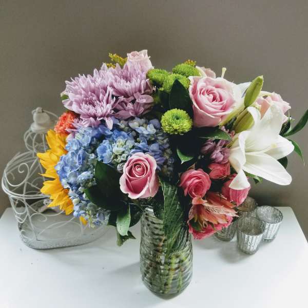 Mixed bouquet of roses, lilies, hydrangeas, and chrysanthemums in a glass vase