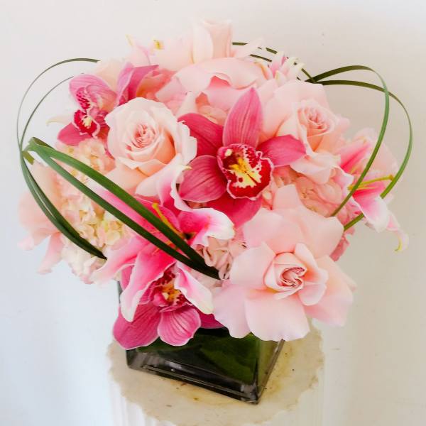 Pink roses and orchids arranged in a square vase