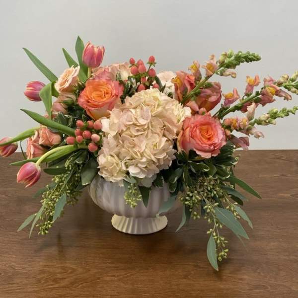 Peach and pink floral arrangement in a white pedestal vase