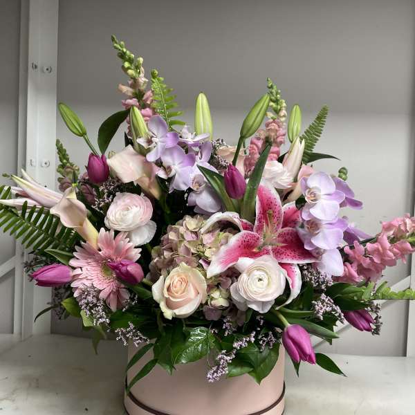 Mixed pink and lavender flower arrangement in a round blush box