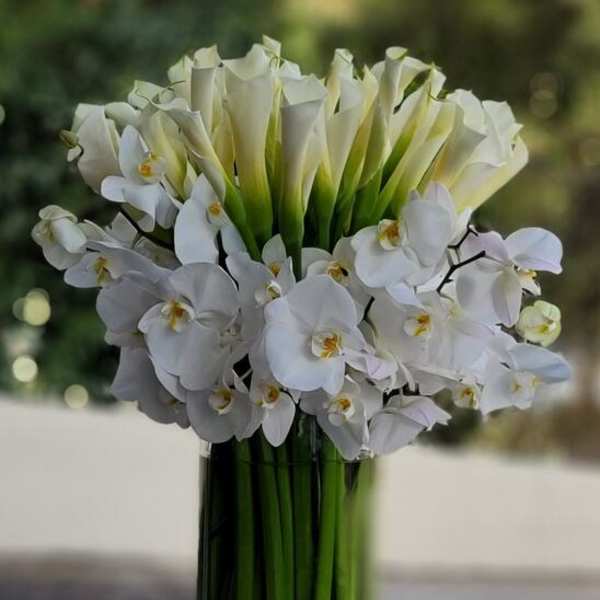 White calla lilies and orchids arranged in a tall glass vase