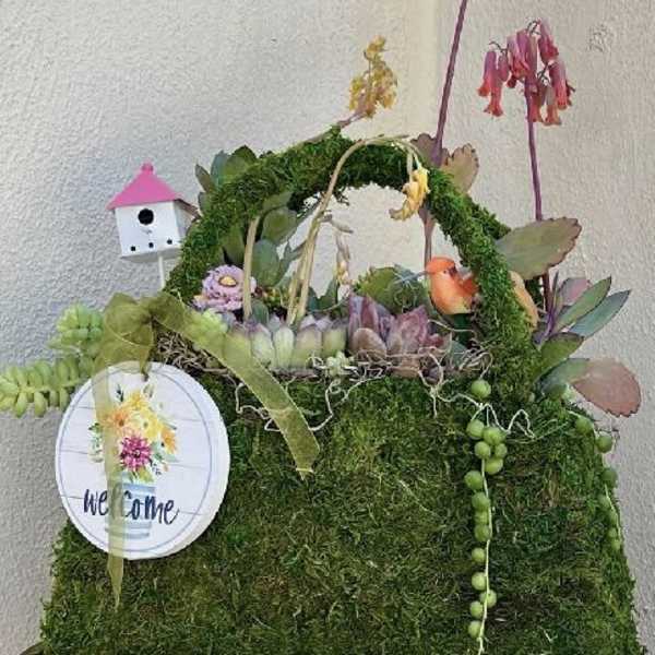 Moss-covered basket with succulents, hanging blooms, and a small birdhouse