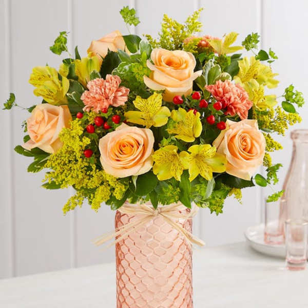 Peach roses and yellow flowers in a pink glass vase