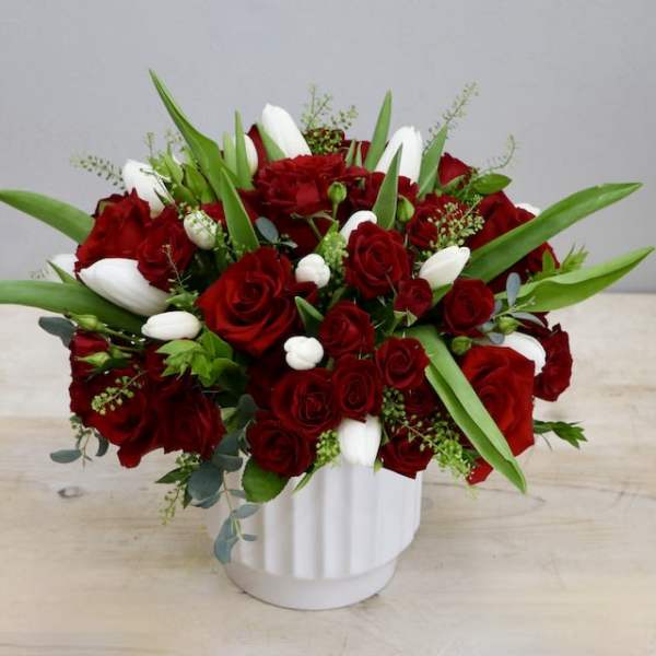 Low red rose and white tulip arrangement in a white ceramic vase