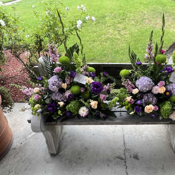 Two floral arrangements on a bench in purple, green, and peach tones