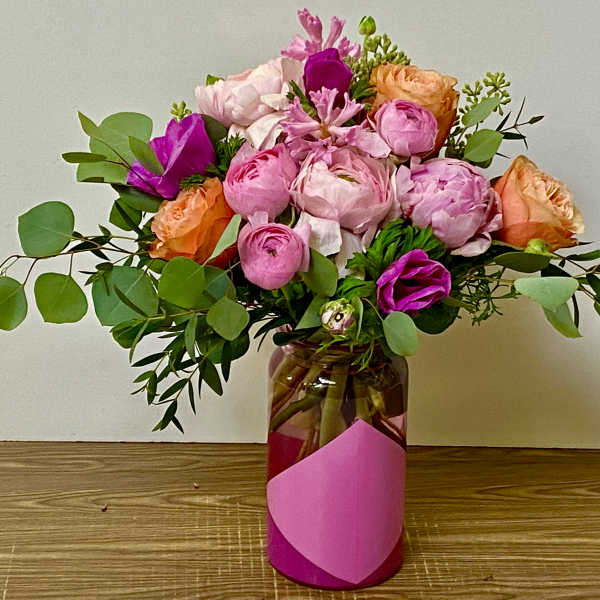 Pink and peach bouquet in a glass vase with trailing greenery