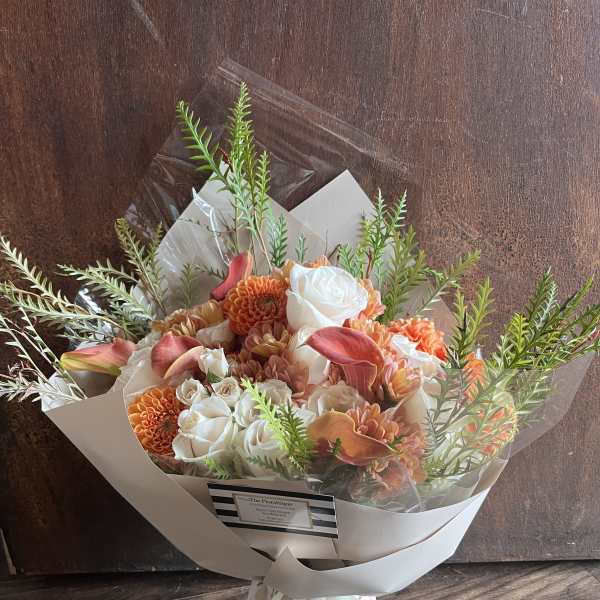 Bouquet of orange and white flowers wrapped in white paper with a ribbon