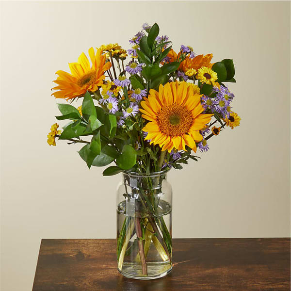 Bouquet of yellow sunflowers and purple daisies in a clear glass vase
