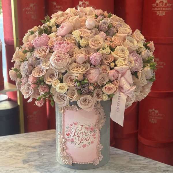 Large pastel rose arrangement in a decorated vase with an "I Love You" plaque