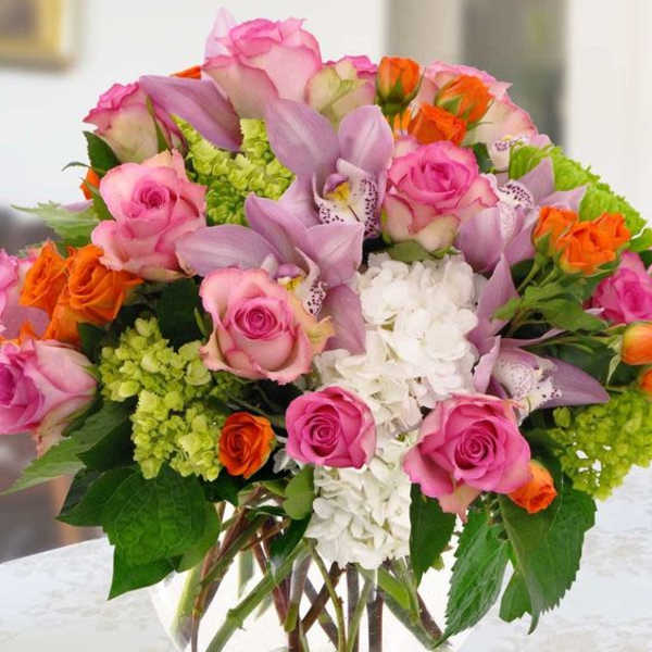 Mixed bouquet of pink roses, lavender orchids, and white hydrangea in a glass vase