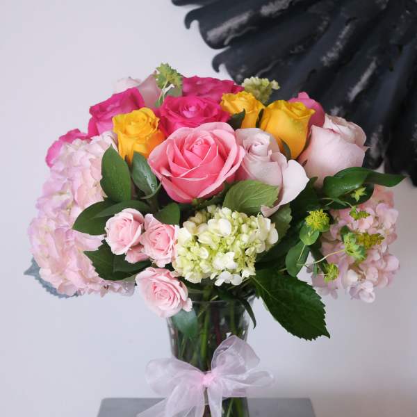 Bouquet of pink, yellow, and white roses in a glass vase with a ribbon