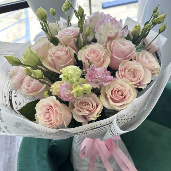 Bouquet of pale pink roses and lisianthus wrapped in paper with a pink ribbon