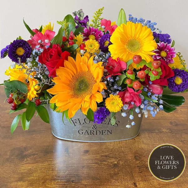 Low galvanized tin arrangement of bright sunflowers, red roses, and mixed colorful blooms