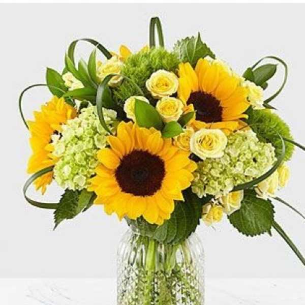 Sunflower bouquet with pale yellow roses in a clear glass vase