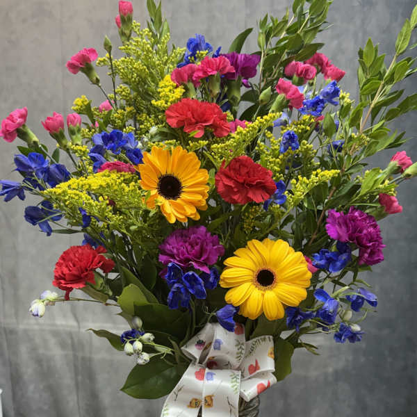 Mixed bouquet in a glass vase with yellow daisies, carnations, and blue flowers