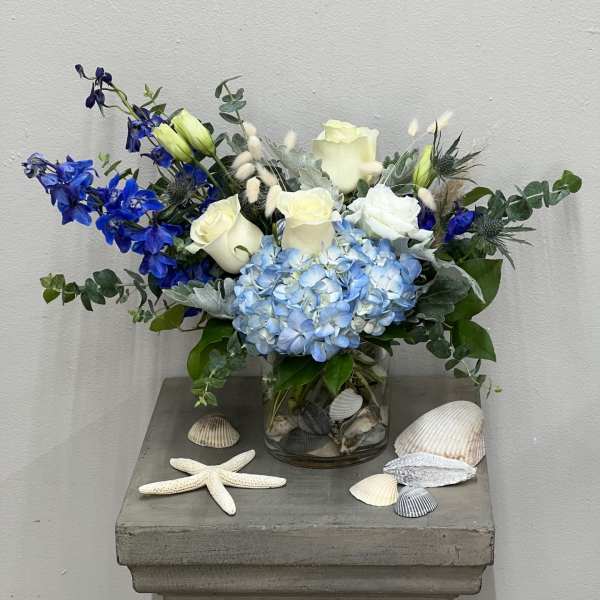Blue and white floral arrangement in a glass vase with seashells and a starfish