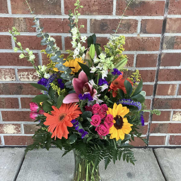 Colorful mixed bouquet in a clear glass vase with lilies, gerberas, roses, and sunflowers