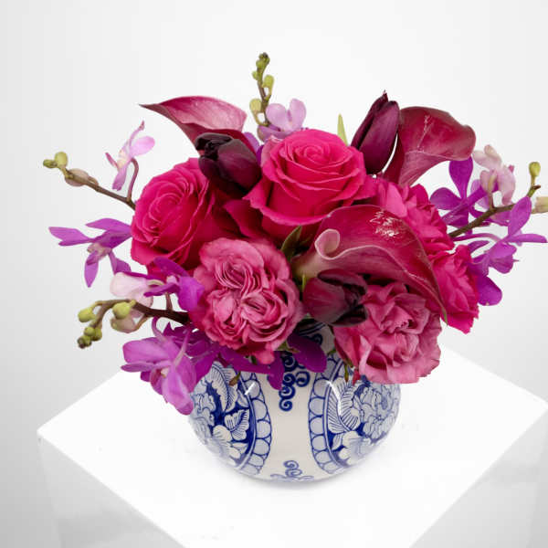 Pink roses and orchids arranged in a blue-and-white ceramic vase.