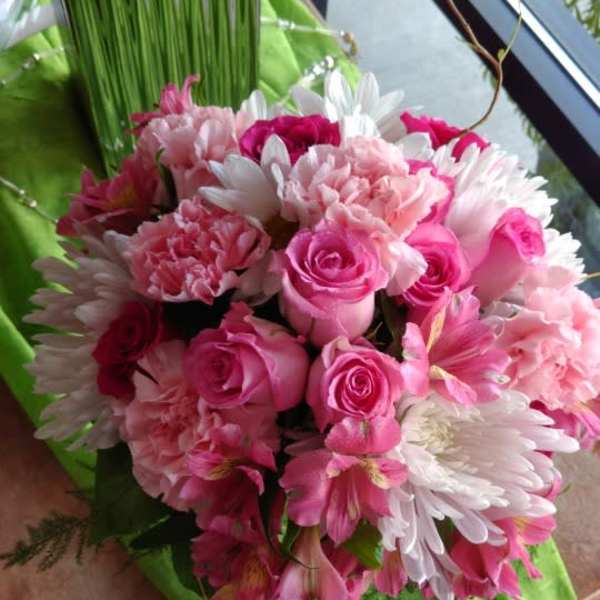 Pink roses and white daisies arranged in a green-wrapped bouquet