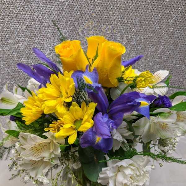 Bouquet of yellow roses, purple irises, and white flowers in a glass vase