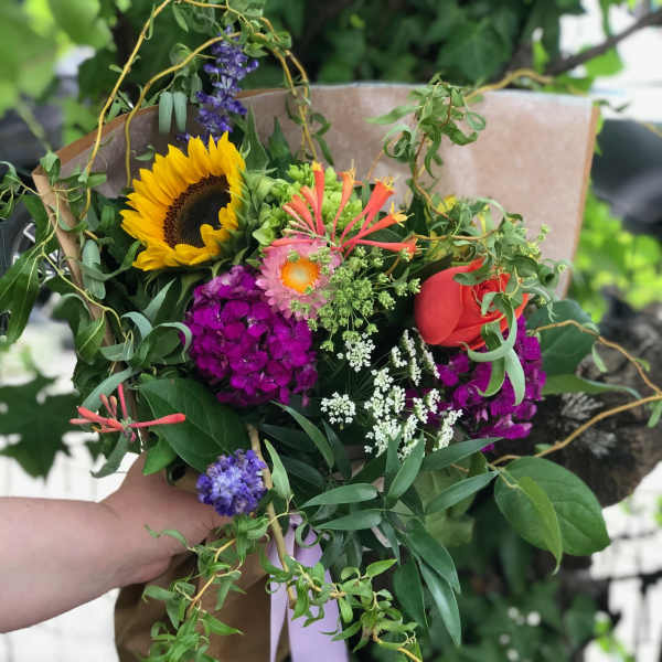 Hand-tied bouquet with a sunflower, red rose, and purple blooms