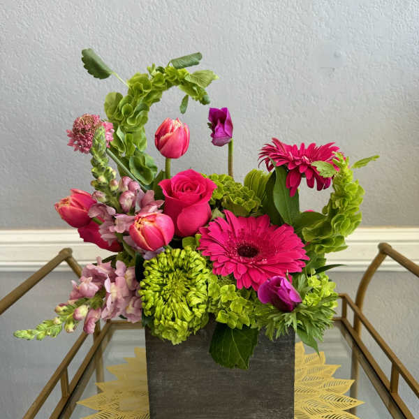 Bright pink and green mixed flower arrangement in a square dark vase