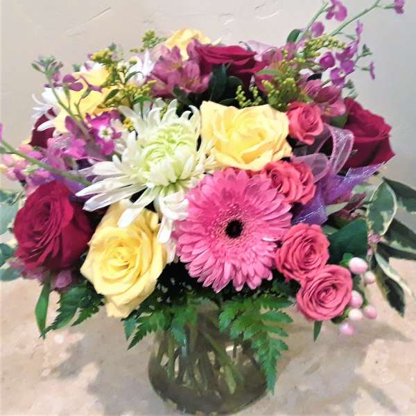 Mixed bouquet of roses, gerbera daisies, and chrysanthemums in a glass vase