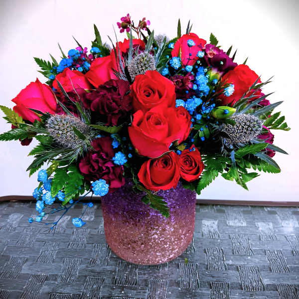Red roses and blue filler flowers in a pink glitter vase